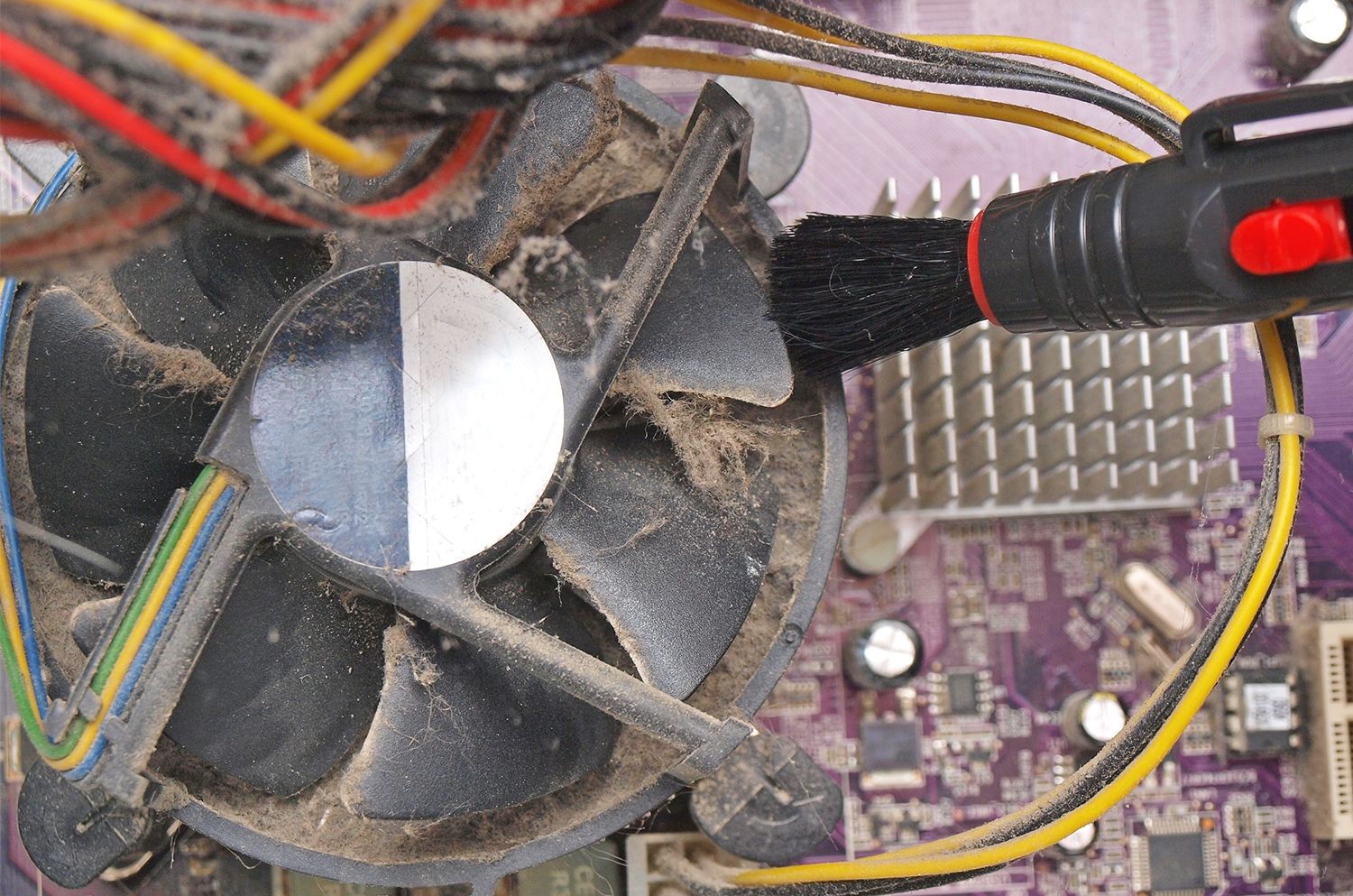Kleine Bürste entfernt Staub und Flusen aus dem freigelegten Lüfter eines Desktop-Computers