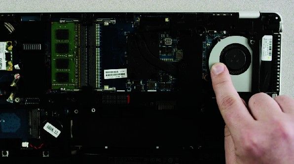 Der Finger einer Person berührt eine unlackierte Metalloberfläche auf der freiliegenden Unterseite eines Laptops, um statische Elektrizität abzuleiten.