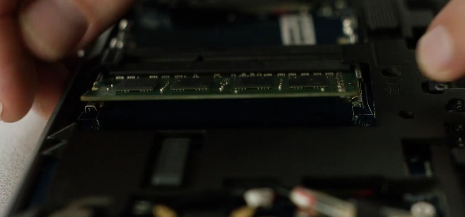 Eine Person löst die Seitenclips eines Crucial RAM-Moduls, um es aus einem Laptop zu entnehmen